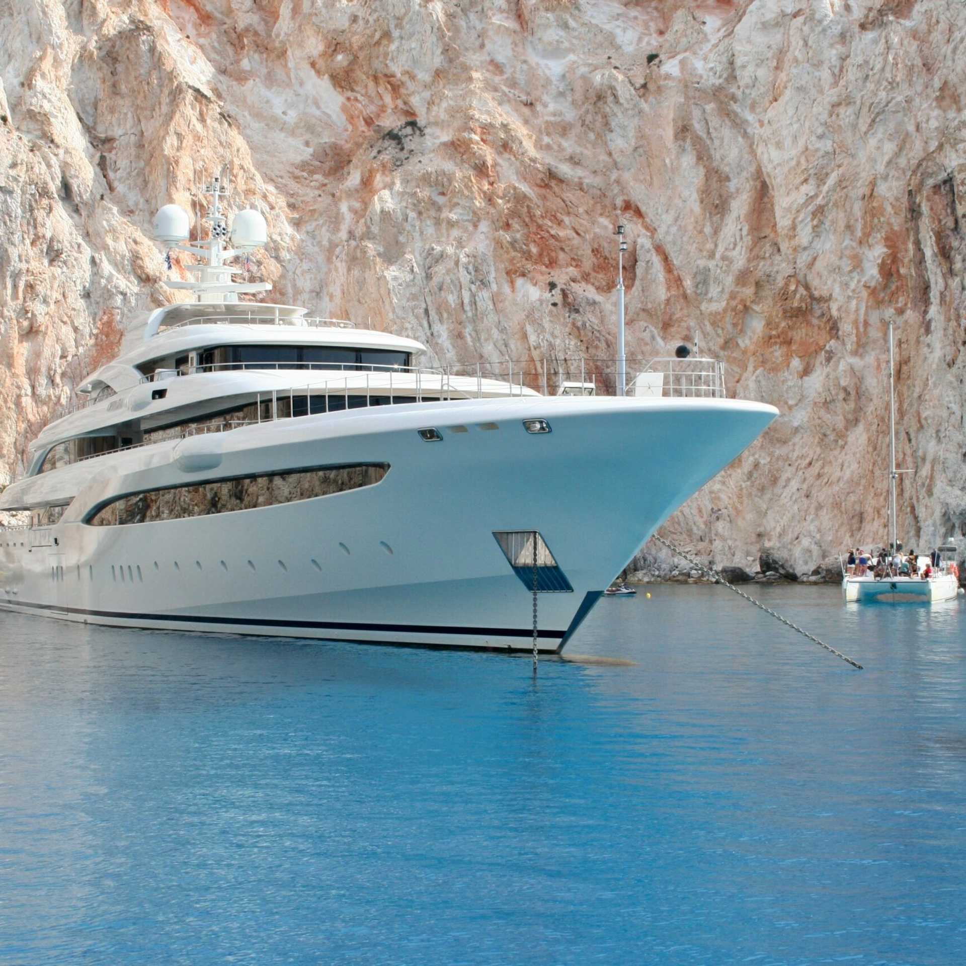 A luxury super yacht anchored near a white coast with crystal blue water.